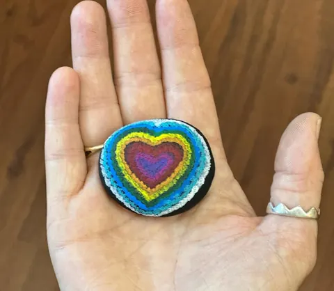 A painted rainbow heart stone resting in an open hand